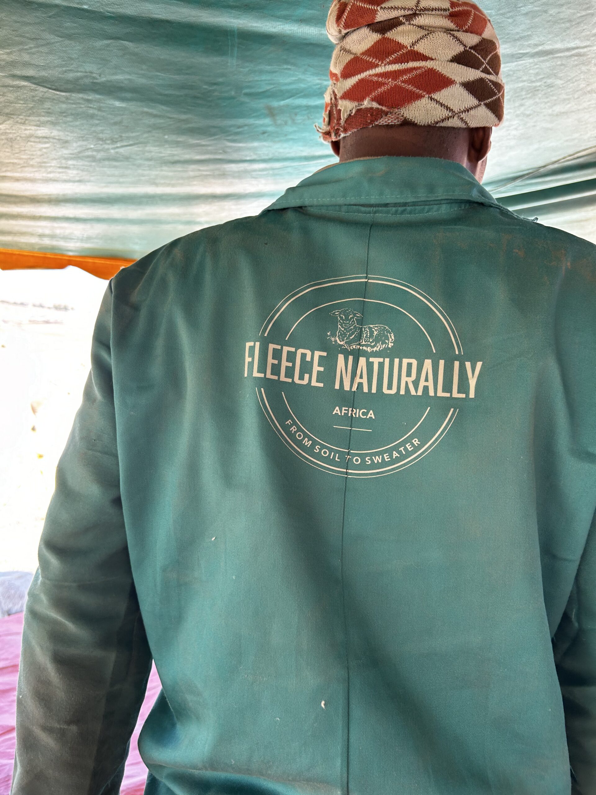 A hand holds a lock of raw wool against a Fleece Naturally Africa branded jacket.