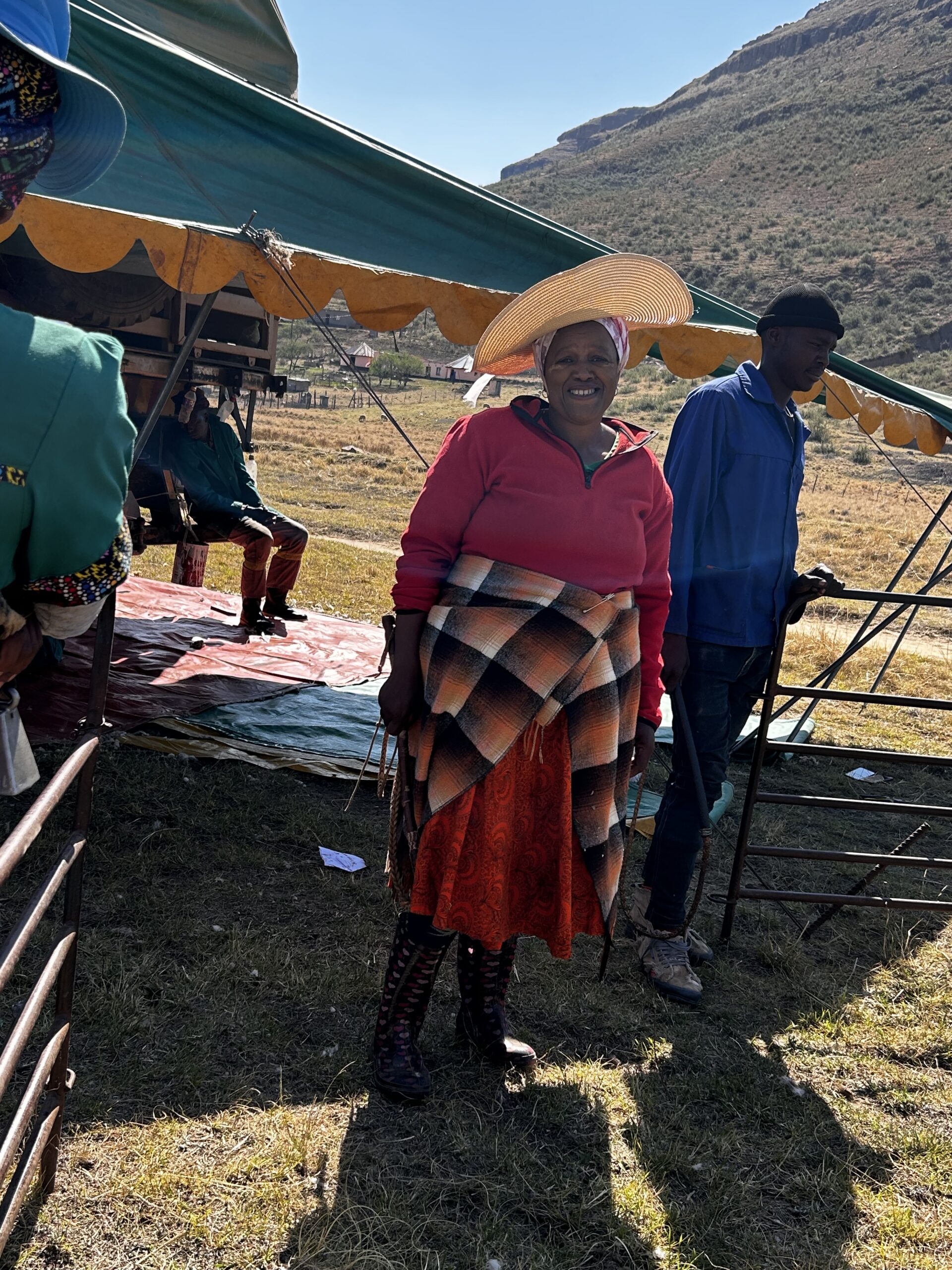 A woman in a sun hat stands at the shearing tent with the mountains behind her.