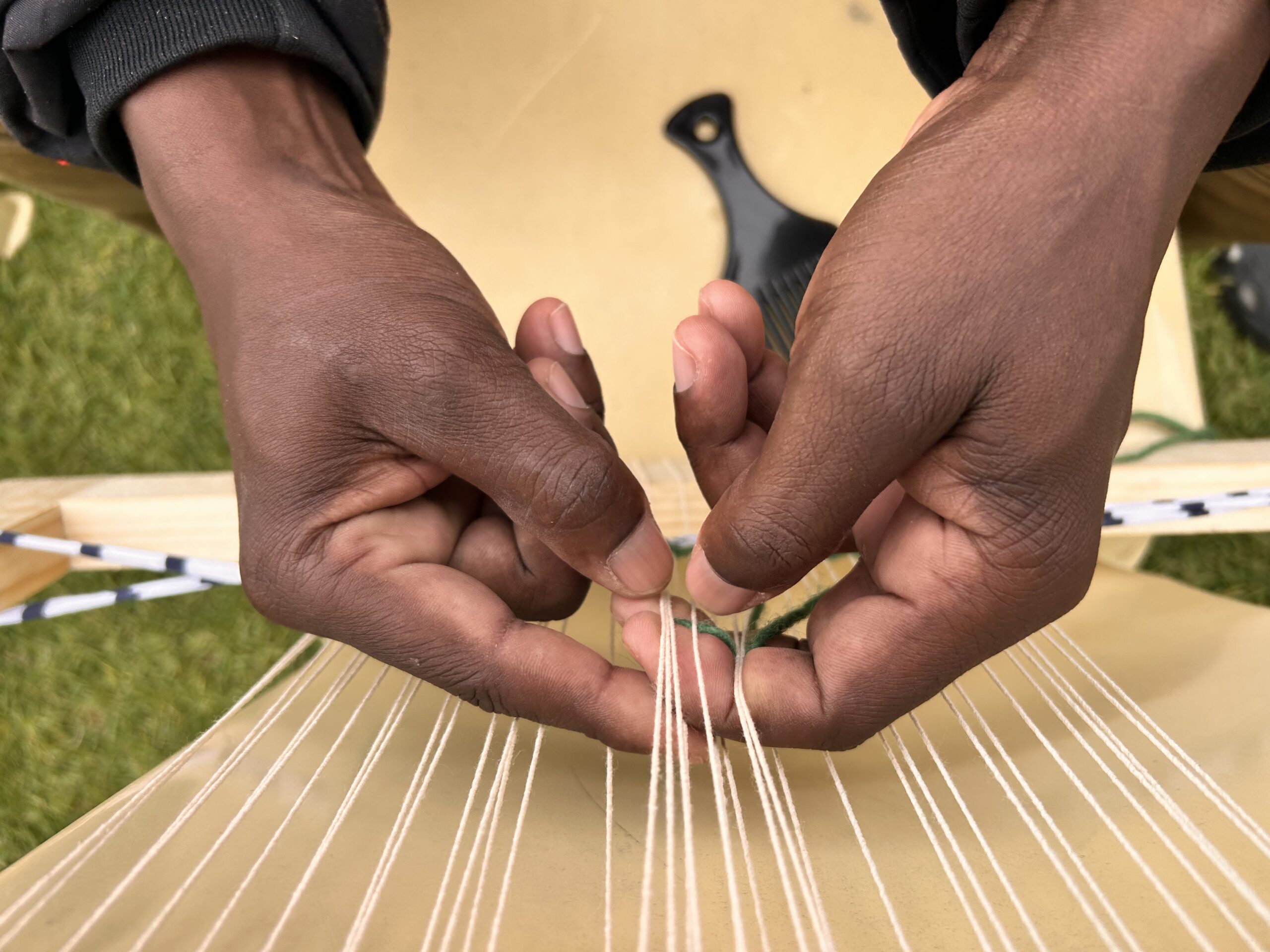 Close-up of hands drawing wool thread across a hand loom.